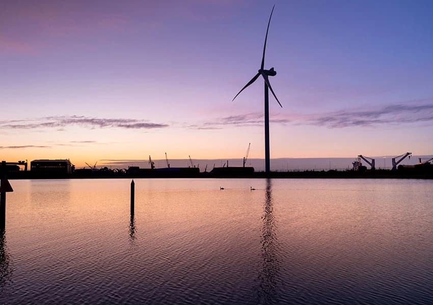 Wind turbines reflected in the water at Odense Harbour at dusk.